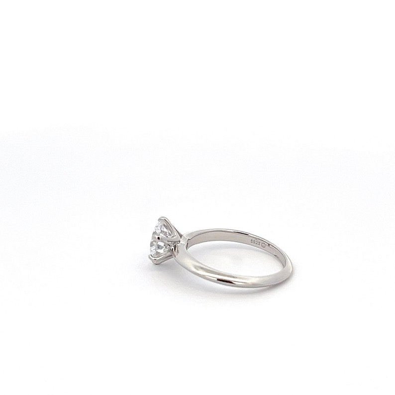 May include: A silver engagement ring with a round, clear diamond. The ring has a simple band and the diamond is set in a four-prong setting.