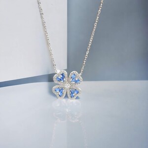 May include: A silver necklace with a blue and white flower pendant. The flower has four petals and is surrounded by small, clear stones.