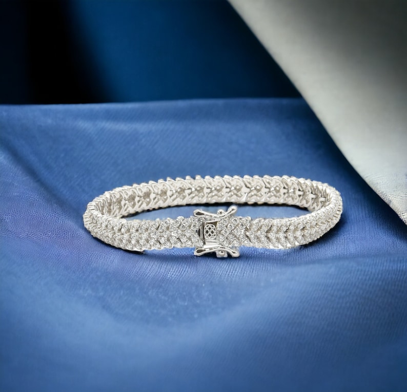 May include: A silver tennis bracelet with a row of small, clear cubic zirconia stones.