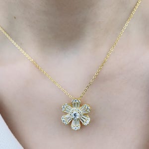 May include: A gold chain necklace with a flower pendant. The flower is made of clear cubic zirconia stones.