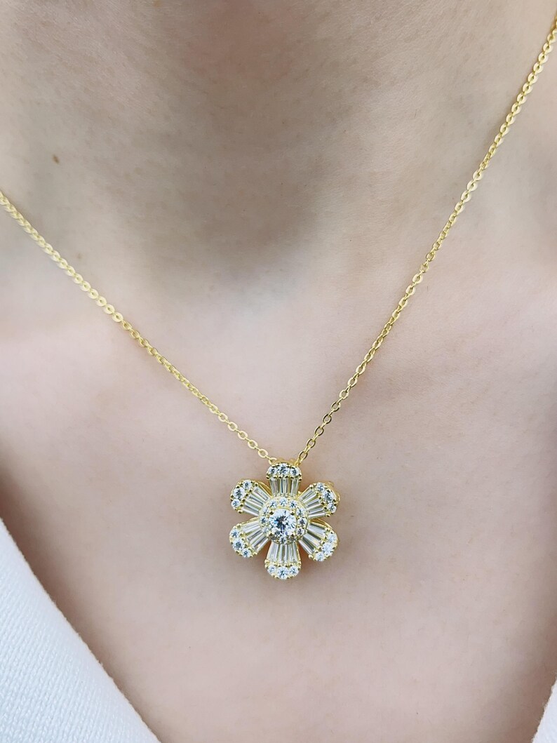 May include: A gold chain necklace with a flower pendant. The flower is made of clear cubic zirconia stones.