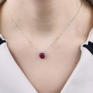 May include: A silver chain necklace with a red gemstone pendant. The pendant is surrounded by smaller clear gemstones.