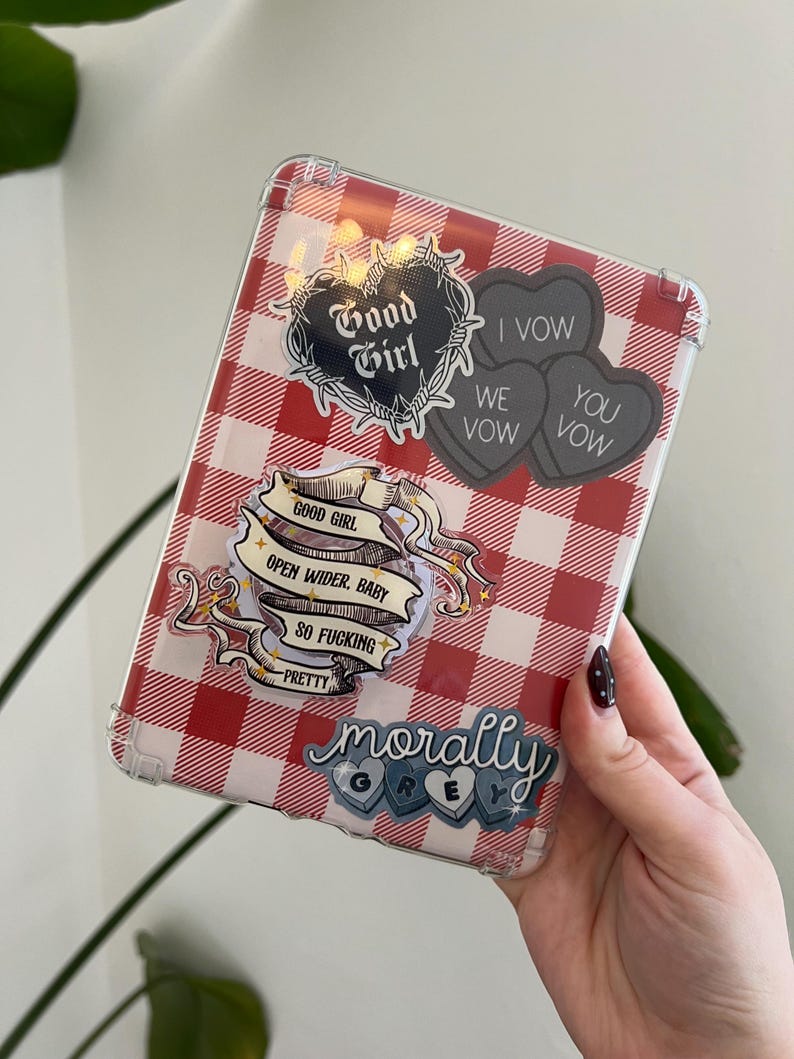 May include: A clear tablet case with a red and white checkered pattern. The case is decorated with stickers that read "Good Girl", "I Vow, We Vow, You Vow", "Open Wider, Baby, So Fucking Pretty", and "Morally Grey".