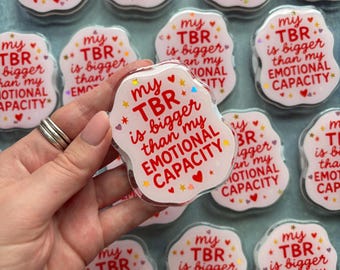 May include: A collection of scalloped-edge acrylic pins featuring the red text 'my TBR is bigger than my EMOTIONAL CAPACITY' accented with small red hearts and yellow stars. The pins have a glossy finish and a white background with a light pink tint.