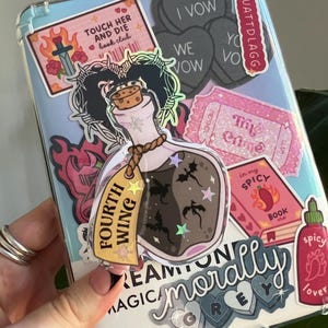 May include: A clear phone case covered in stickers. Stickers include a potion bottle with the text "Fourth Wing", a pink book with "Spicy Book Club", and heart-shaped stickers with "I Vow" and "We Vow".