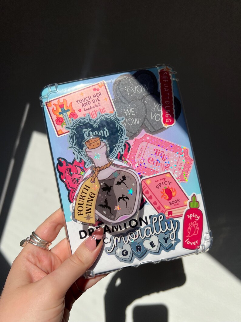 May include: A clear phone case decorated with stickers. Stickers include text that says "Touch Her and Die book club", "I Vow", "We Vow", "Try Crime", "Fourth Wing", "In my Spicy Book", and "Spicy Lover".