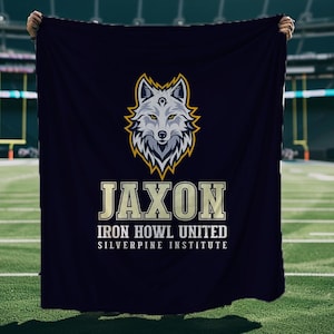 Może przedstawiać: Granatowy koc z logo głowy wilka ze złotymi i białymi akcentami. Tekst "JAXON" jest wyświetlany nad "IRON HOWL UNITED SILVERPINE INSTITUTE" złotymi literami. Koc jest prezentowany przed stadionem piłkarskim.