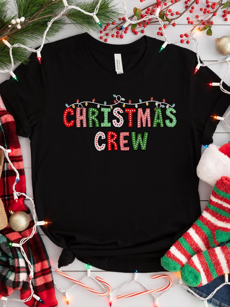 May include: Black t-shirt with the text "Christmas Crew" in colorful letters with white string lights above the text. The letters are decorated with small white dots.