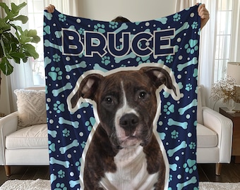May include: A blue and white fleece blanket with a bone and paw print pattern. The blanket features a dog's face and the name "Bruce" in bold white letters.