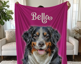 May include: A pink fleece blanket with a Bernese Mountain Dog's face printed on it. The dog is looking at the camera with its tongue sticking out. The name "Bella" is printed in white cursive above the dog's face.