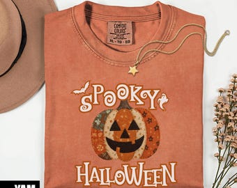 Puede incluir: Camiseta naranja Comfort Colors con un diseño de "Spooky Halloween" con una calabaza de patchwork, un murciélago y un fantasma. Un collar con colgante de estrella dorada descansa sobre la camisa. Talla XL-TG-EG.