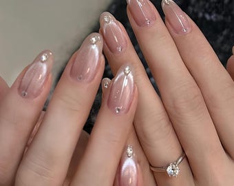 Op de afbeelding: Close-up van handen met naakte, ovale nagels met een glinsterende afwerking en kleine strass steentjes. De nagels hebben een witte punt met een dunne glitterstreep.
