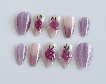 May include: Set of ten false nails with a gradient design. The nails are oval shaped and have a light pink base with a shimmery purple tip. Some of the nails have a 3D grape design.