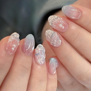 Könnte beinhalten: Ovale Gel-Nageldesign mit einem Farbverlauf von Rosa und Blau. Einige Nägel haben 3D-Muschelverzierungen mit kleinen Perlenakzenten, die eine zarte, vom Meer inspirierte Ästhetik schaffen.