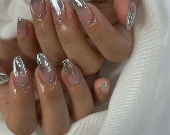 May include: Close-up of a hand with long, clear, silver-tipped nails with small rhinestones on each nail.