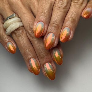 May include: Close-up of hands with oval-shaped nails painted with a gradient of orange and iridescent shimmer.