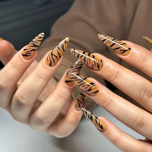 May include: Close-up of long, pointed nails with a tiger stripe design in black and orange.