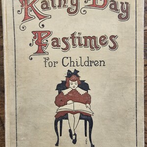 May include: A vintage book cover with the title "Rainy Day Pastimes for Children" in red and black lettering. The cover features a black and white illustration of a girl sitting in a chair reading a book.