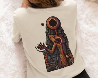 May include: Cream-colored t-shirt featuring a colorful, stylized illustration on the back. The artwork depicts a figure with a large, circular head and long hair, with a ball floating nearby. The design incorporates shades of orange, purple, and blue.