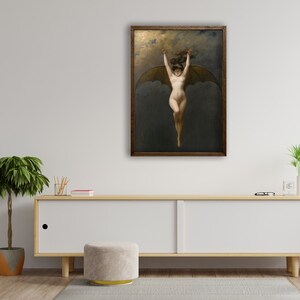 May include: A framed artwork depicts a nude figure with bat-like wings, arms raised, against a dark, cloudy background. The artwork is in a wooden frame and hangs on a white wall above a wooden cabinet. The overall aesthetic is classical.