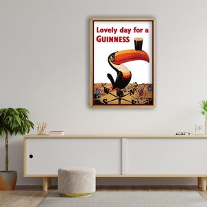 K&ouml;nnte beinhalten: Gerahmte Guinness-Werbung mit einem Tukan mit gro&szlig;em orange-roten Schnabel, der ein Pint Guinness h&auml;lt. Der Text "Lovely day for a Guinness" ist rot. Der Hintergrund zeigt eine Stadtlandschaft.