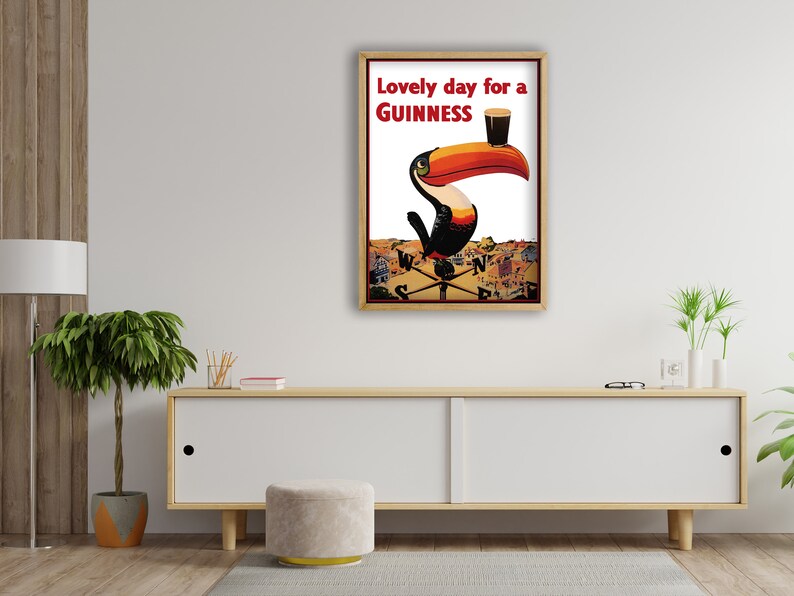 K&ouml;nnte beinhalten: Gerahmte Guinness-Werbung mit einem Tukan mit gro&szlig;em orange-roten Schnabel, der ein Pint Guinness h&auml;lt. Der Text "Lovely day for a Guinness" ist rot. Der Hintergrund zeigt eine Stadtlandschaft.