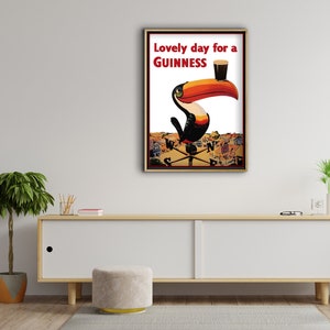 K&ouml;nnte beinhalten: Gerahmtes Vintage-Guinness-Werbeplakat mit einem Tukan mit gro&szlig;em orange-schwarzem Schnabel, der ein Pint Guinness h&auml;lt. Der Text lautet "Lovely day for a Guinness". Das Kunstwerk ist vor einem wei&szlig;en Hintergrund.