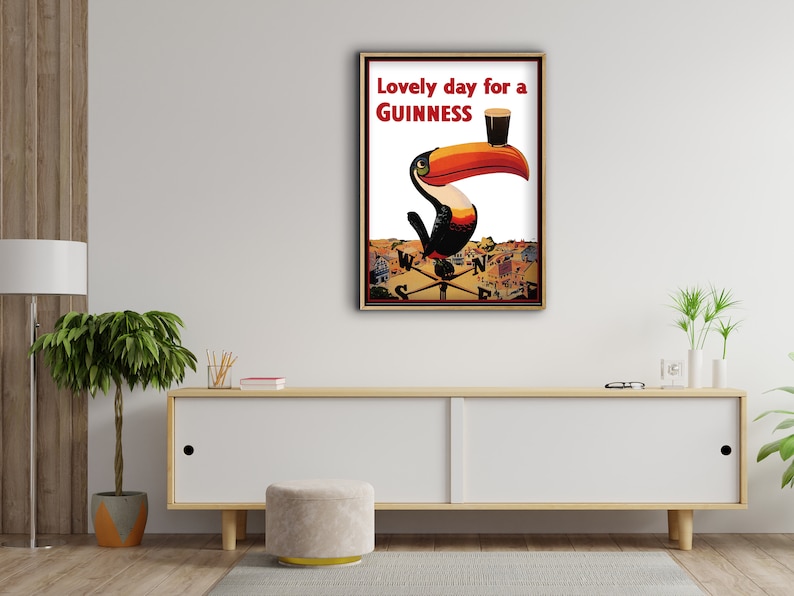 K&ouml;nnte beinhalten: Gerahmtes Vintage-Guinness-Werbeplakat mit einem Tukan mit gro&szlig;em orange-schwarzem Schnabel, der ein Pint Guinness h&auml;lt. Der Text lautet "Lovely day for a Guinness". Das Kunstwerk ist vor einem wei&szlig;en Hintergrund.