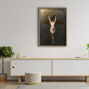 May include: A framed artwork depicting a nude figure with bat wings, arms raised, against a dark, cloudy background. The painting has a gold frame and is displayed on a white cabinet in a room with wood paneling and a potted plant.