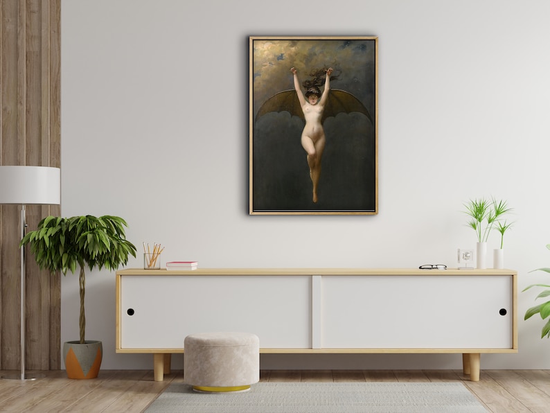 May include: A framed artwork depicting a nude figure with bat wings, arms raised, against a dark, cloudy background. The painting has a gold frame and is displayed on a white cabinet in a room with wood paneling and a potted plant.