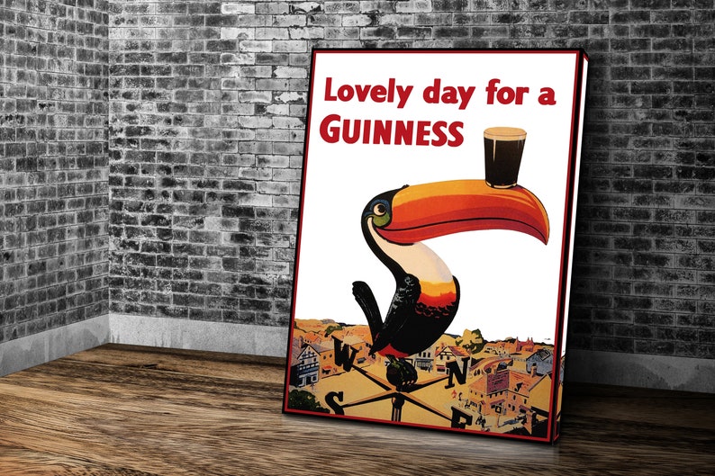 K&ouml;nnte beinhalten: Ein gerahmtes Guinness-Poster mit einem Tukan, der ein Pint Guinness h&auml;lt. Der Text "Lovely day for a Guinness" ist rot. Der Tukan hat einen gro&szlig;en orange-roten Schnabel. Der Hintergrund zeigt eine Stadt und einen Kompass.
