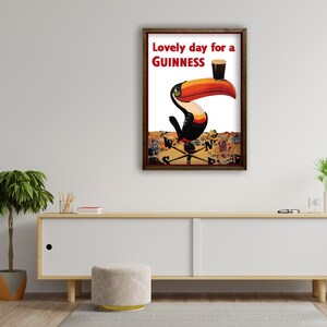 K&ouml;nnte beinhalten: Ein gerahmtes Guinness-Werbeplakat mit einem Tukan, der ein Pint Guinness h&auml;lt. Der Text "Lovely day for a Guinness" ist rot. Der Tukan hat einen gro&szlig;en orange-schwarzen Schnabel. Der Hintergrund zeigt eine Stadt.