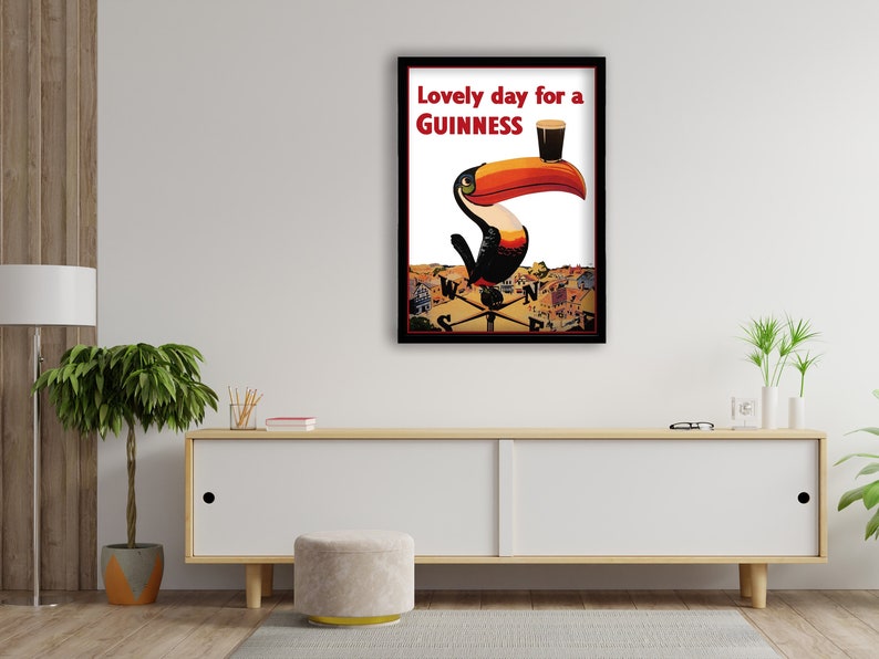 K&ouml;nnte beinhalten: Gerahmtes Guinness-Poster mit einem Tukan mit gro&szlig;em orangefarbenem Schnabel, der ein Pint Guinness h&auml;lt. Der Text "Lovely day for a Guinness" ist rot. Das Kunstwerk ist vor wei&szlig;em Hintergrund.