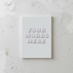May include: A rectangular, pale grey card featuring the embossed text "YOUR WORDS HERE" in a 3D, bubble-style font. The card is set against a textured, off-white backdrop.