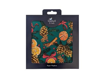 May include: A package of paper napkins with a festive Christmas design. The napkins feature a dark green background with illustrations of pine cones, orange slices, cinnamon sticks, and red bows. The brand name "bluebell & lark" is visible.
