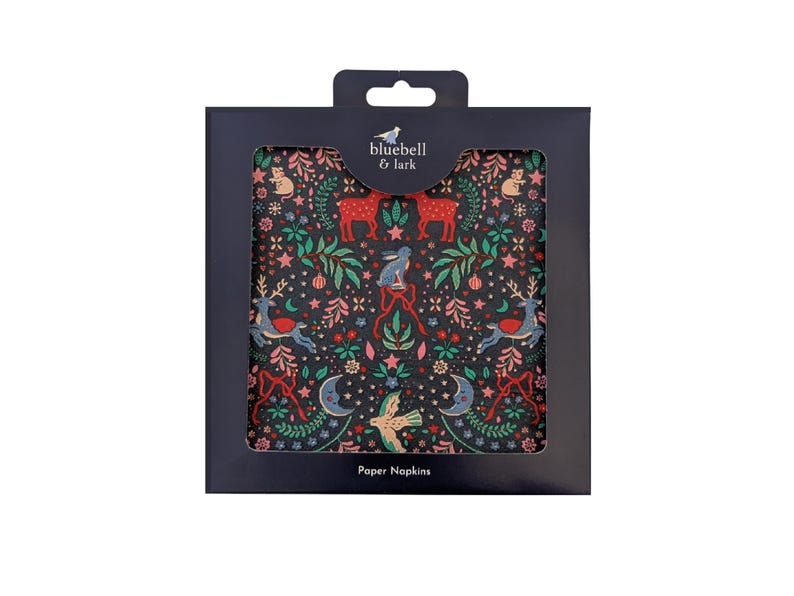 May include: A pack of paper napkins featuring a dark background with a forest-themed pattern. The design includes deer, rabbits, birds, and crescent moons in red, green, and blue. The package has the text "bluebell & lark" and "Paper Napkins".