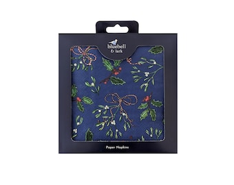 May include: A package of navy blue paper napkins with a festive design. The napkins feature a pattern of holly leaves, red berries, and decorative bows. The package is labeled "Paper Napkins" and includes the "bluebell & lark" logo.