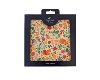 May include: A box of paper napkins with a colorful floral and woodland animal design. The napkins feature illustrations of squirrels, foxes, and flowers in shades of orange, pink, and blue. The brand name "bluebell & lark" is printed on the box.