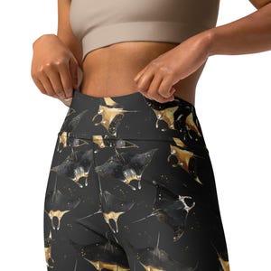 Op de afbeelding: Zwarte leggings met een herhalend patroon van gouden mantaroggen op een zwarte achtergrond.