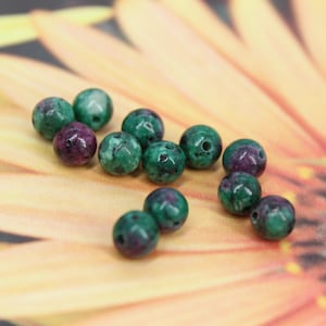 May include: A collection of green and purple gemstone beads. The beads are round and have a mottled appearance.