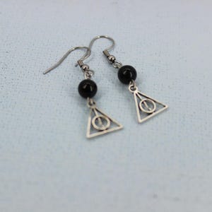 May include: A pair of silver earrings with black beads and a triangle charm with a circle inside. The charm is a symbol from the Harry Potter series.