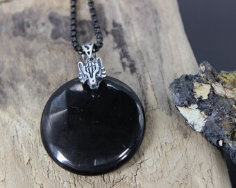 May include: A black, circular pendant with a silver wolf head design, suspended from a black chain. The pendant is smooth and reflective, set against a wooden background. A unique piece of jewelry.