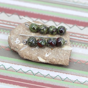 May include: A pair of earrings with green and red gemstone beads on silver wire.