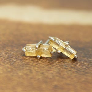 May include: A pair of silver earrings with small, rectangular, light brown gemstones.