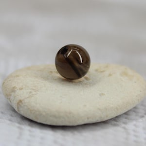 May include: A brown and black striped glass bead resting on a white rock.