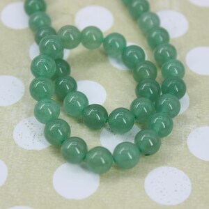 May include: A strand of smooth, round, translucent green beads arranged in a circular loop. Each bead features a polished surface with subtle variations in color and internal texture, reflecting light across the spherical shapes of the gemstone strand.