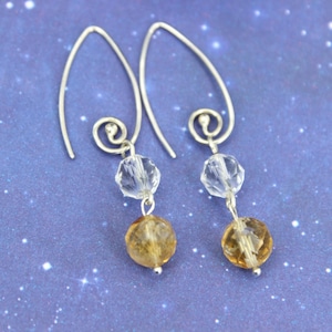 May include: A pair of silver dangle earrings with a clear crystal bead and a brown faceted bead on each earring.
