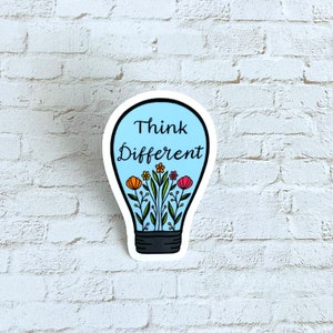 May include: A sticker in the shape of a lightbulb with the words "Think Different" in black script. Inside the lightbulb are colorful flowers with orange, yellow, and red petals. The background is a light blue color.