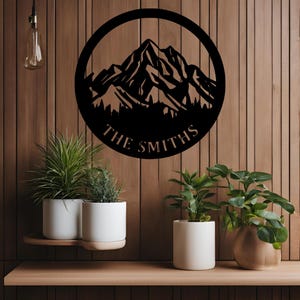 Peut inclure: Décoration murale en métal noir représentant une silhouette de montagne avec un cercle autour et le texte "THE SMITHS" en bas.