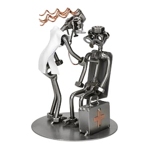 Puede incluir: Escultura metálica que representa a un médico examinando a un paciente. El médico, hecho de tuercas y tornillos metálicos, lleva una bata blanca y sostiene un estetoscopio. El paciente está sentado en una silla, con un maletín metálico con una cruz de cobre.